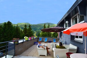A terrace with outdoor seating, a view of green hills, and a building with a window. - Parking, tv, ski locker, 25m², Super Besse (Super Besse)