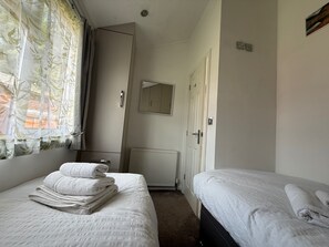 Een slaapkamer met twee bedden, een radiator, een deur en een raam met gordijnen.