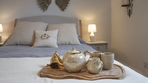 A neatly made bed with a wooden tray holding a teapot, cups, and a dried fruit. - Antelope Cottage - Northleach, Cotswolds - near pubs (Northleach)