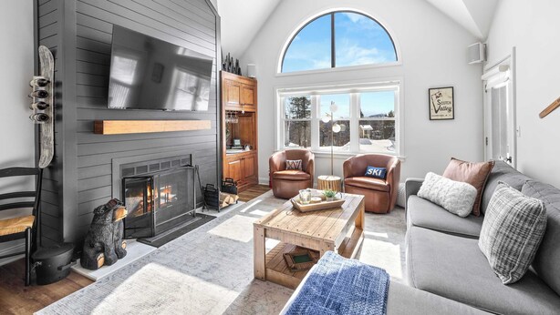 A cozy living room with a fireplace, leather chairs, a sofa, and a large window offering a view of the outdoors. - Apres Chalet: Winterplace Ski-in/Out pool+hot tubs (Ludlow)