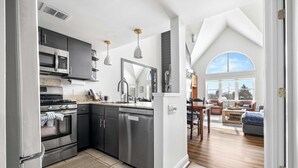 A modern kitchen with stainless steel appliances, a large mirror, and a dining area with a view of the outdoors. - Apres Chalet: Winterplace Ski-in/Out pool+hot tubs (Ludlow)
