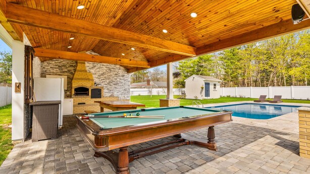 Un espace extérieur avec une piscine, une table de billard, une cheminée en pierre et un coin barbecue en briques.