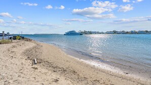 Une plage avec un yacht sur l’eau et des maisons en arrière-plan.