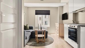 A compact kitchen with a built-in oven, a dining area with a round table and two chairs, a grey sofa, and a window with a dark blind. - Cozy Studio in Bergen Center (Bergen)