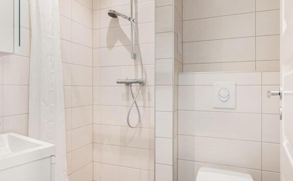 Een moderne badkamer met witte tegels, een douche en toilet.