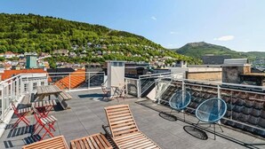 A rooftop terrace with lounge chairs, a table, and a view of a hillside town. - Cozy Studio in Bergen Center (Bergen)