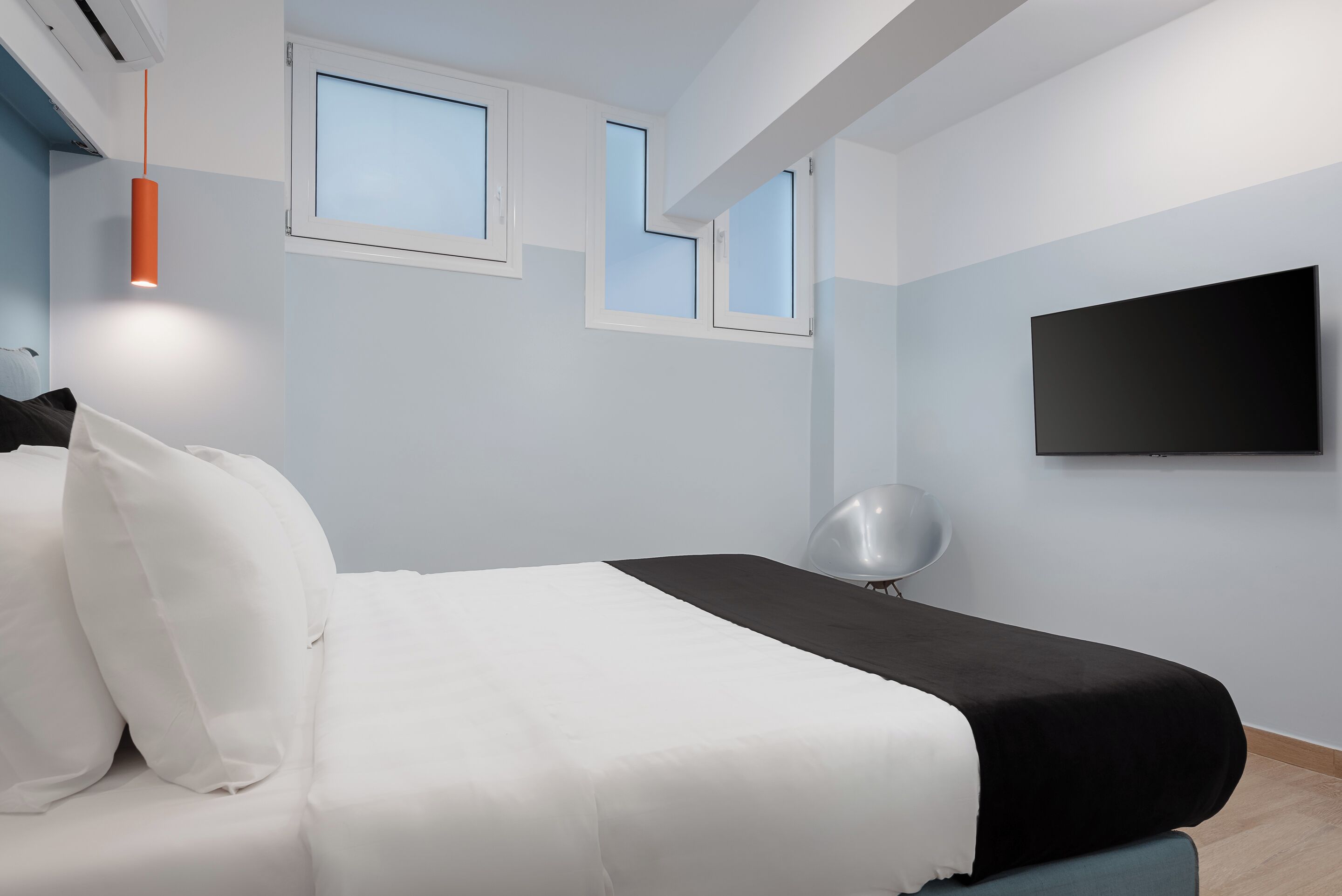 A modern bedroom with a bed, white and black bedding, a flat-screen TV, and a unique window design.