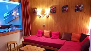 A cozy room with a wooden wall, a red sofa, a wooden table, and a window with curtains. - 70m from ski slopes, 3rd floor, view ski slopes, balcony, tv, 27m², Méribel-Mottaret (Méribel - Les Allues)