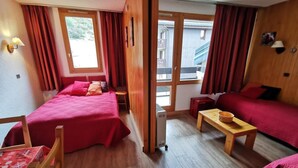 A room with two beds, a wooden table, and a sofa. - 70m from ski slopes, 3rd floor, view ski slopes, balcony, tv, 27m², Méribel-Mottaret (Méribel - Les Allues)