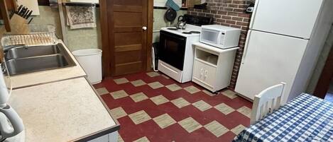 Una cucina compatta con pavimento a scacchi rossi e bianchi, pensili e basi bianche, un forno a microonde, un fornello e un frigorifero.