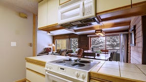 A kitchen with a stove, cabinets, and a window overlooking a snowy landscape. - An202 Anaconda 2br 2ba 2 Bedroom Condo (Copper Mountain)