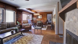 A cozy living room with a fireplace, wooden walls, a ceiling fan, and a dining area with wooden furniture. - An202 Anaconda 2br 2ba 2 Bedroom Condo (Copper Mountain)