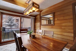 Un intérieur en bois avec une table à manger, des chaises, une plante en pot et un grand miroir au mur.