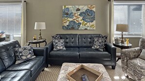 Een woonkamer met een zwarte leren bank, een gestreept voetenbankje en een schilderij aan de muur.