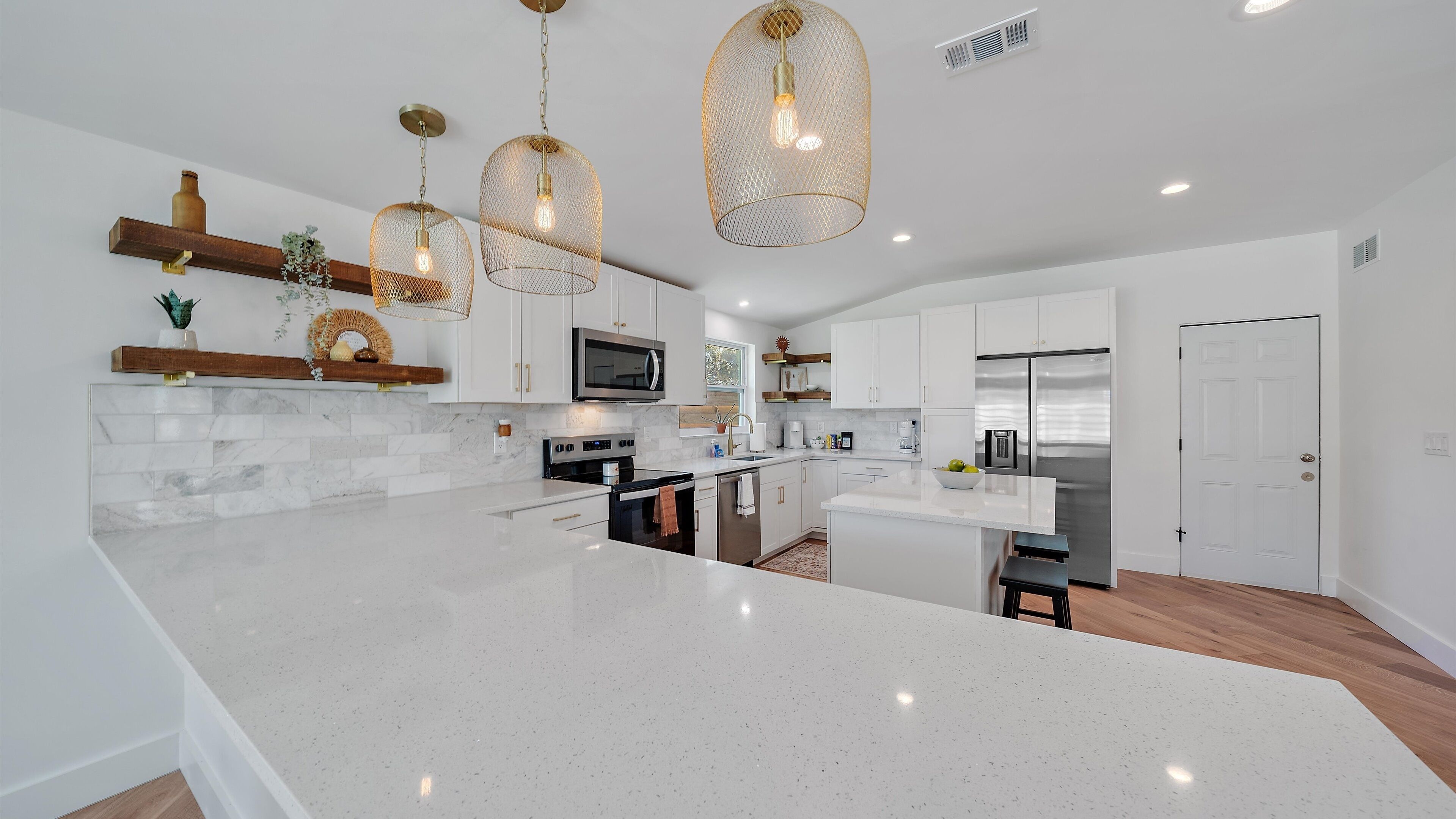 Une cuisine moderne avec des meubles blancs, un grand îlot central, des appareils en acier inoxydable et des luminaires suspendus.