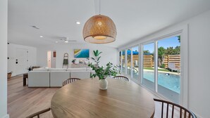 A modern living room with a wooden dining table, white sofa, and large windows overlooking a swimming pool. - Coastal Cottage 2 Bedroom Home (Sarasota)