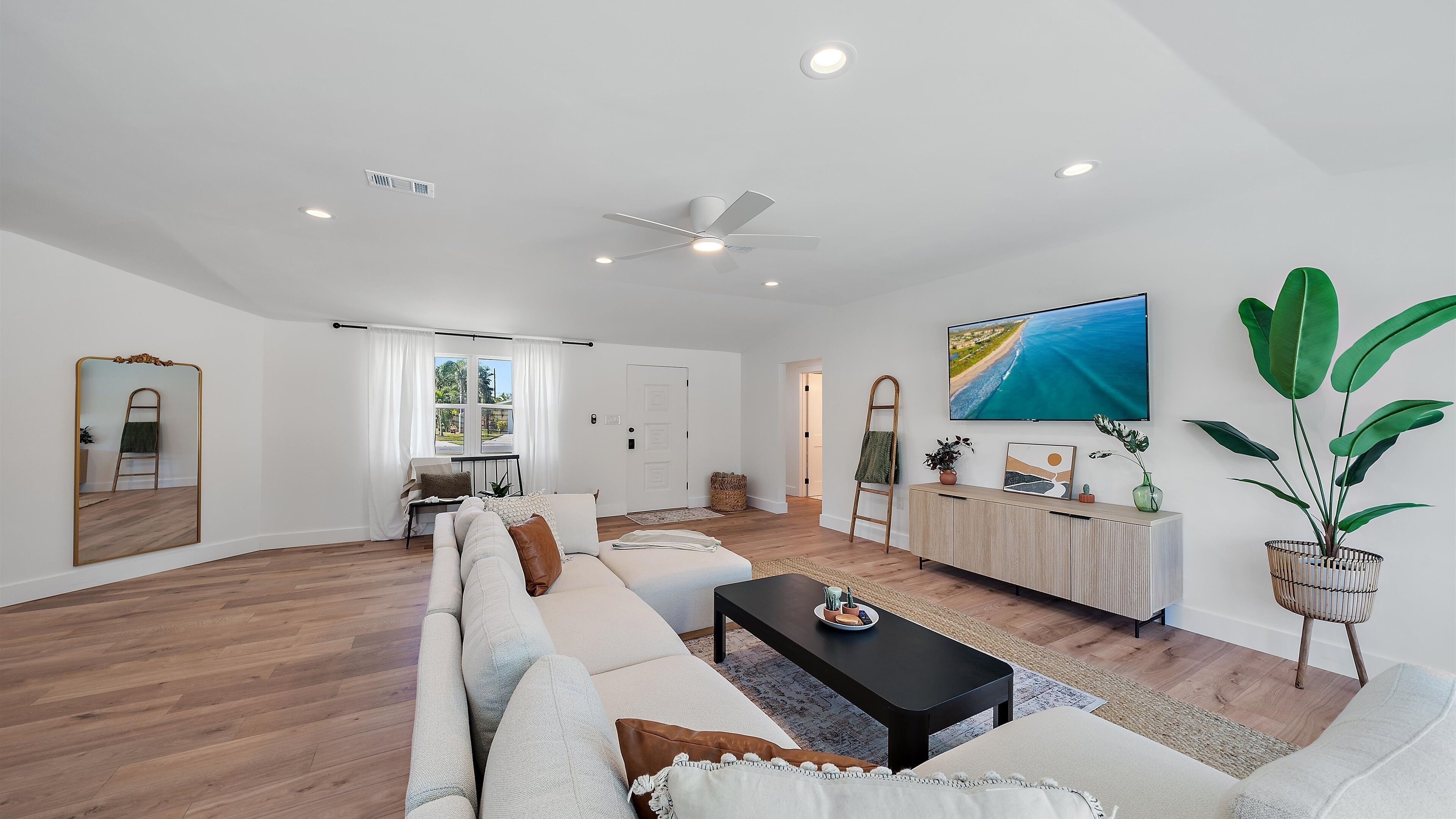 A spacious living room with a large sofa, a coffee table, and a TV mounted on the wall.