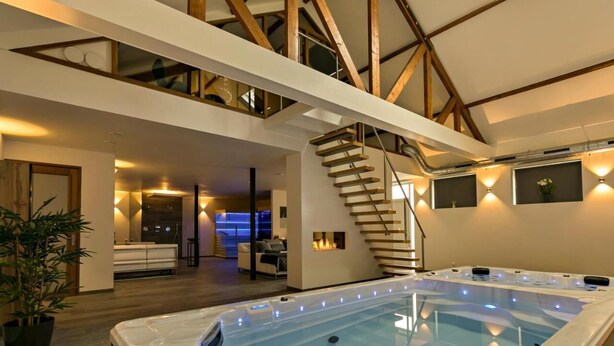 A modern interior with a hot tub, wooden beams, a staircase, and a cozy seating area. - Waal Wellness Villa Maas and Waal Wellness & Suites (Dreumel)