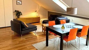 A modern loft apartment with a dining area, a sofa, a small table, and a plant. - City-Center Apartment with Loggia and Parking (Würzburg)