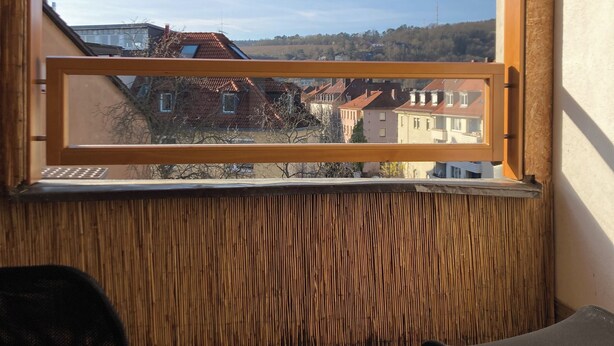 A balcony with a view of a residential area, a wooden floor, and two chairs. - City-Center Apartment with Loggia and Parking (Würzburg)
