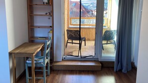 A small room with a wooden desk, a chair, a bookshelf, and a sliding glass door leading to an outdoor balcony with a chair. - City-Center Apartment with Loggia and Parking (Würzburg)