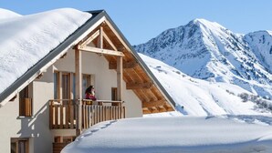 Een chalet met een houten balkon, een berg op de achtergrond en besneeuwde omgeving.