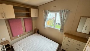 Un dormitorio pequeño con una cama litera, una mesita de noche, un armario y una ventana con cortinas.