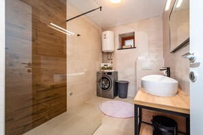 A modern bathroom with a wooden shower enclosure, a built-in washing machine, a sink, and a mirror. - Villa Mendula Zadar Villas (Novigrad)