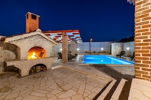 An outdoor area with a stone fireplace, a pool, and seating areas. - Villa Mendula Zadar Villas (Novigrad)
