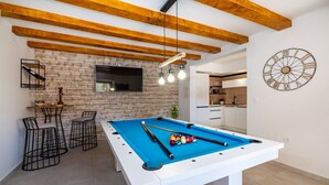A pool table with a blue felt surface, surrounded by black wireframe chairs, in a room with exposed wooden beams and a brick wall. - Villa Mendula Zadar Villas (Novigrad)