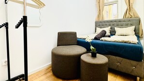 A modern bedroom with a bed, two ottomans, a standing exercise bike, and a window with curtains. - Cozy Rooms Superb Location near Augarten (Vienna)