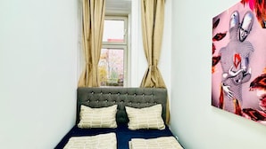 A narrow room with a bed, a window with curtains, and a painting on the wall. - Cozy Rooms Superb Location near Augarten (Vienna)