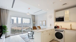 A modern kitchen with a large window, a dining area with a view, and a washing machine. - Livbnb-Modern Living 1B Apartment in JVC (Dubai)