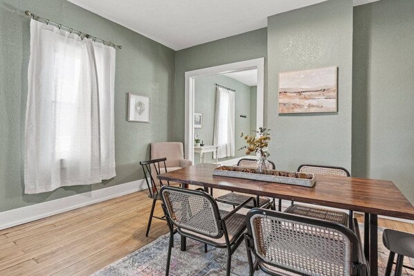 A dining area with a wooden table, chairs, and a vase with dried flowers.