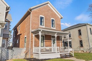 A two-story brick house with a porch, a small front yard, and a neighboring building.