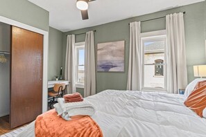 A bedroom with a bed, a desk, a chair, and a window with curtains.