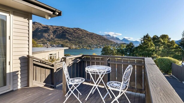 Une terrasse avec deux chaises en métal blanc et une petite table ronde, offrant une vue sur un lac et des montagnes.