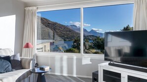 Une chambre d’hôtel moderne dotée d’une grande fenêtre donnant sur les montagnes, d’un canapé, d’une petite table et d’un téléviseur à écran plat posé sur un meuble blanc.