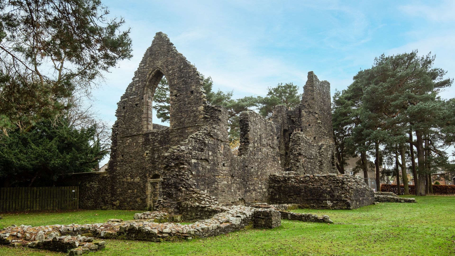 The ruins of a stone structure with multiple arches and columns, surrounded by trees and a grassy area.