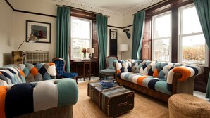 A cozy living room with a striped sofa, a vintage suitcase, and a classic chair. - Dalgety, Peebles - sleeping 8 guests in 4 bedrooms (Peebles)