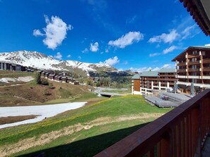 A mountain resort with a view of snow-capped peaks, a river, and a wooden building with balconies.