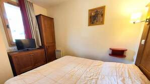 Ein Hotelzimmer mit einem großen Bett, einem Holzschrank, einem Fernseher auf einem Schreibtisch, einem Bild an der Wand und einem roten Regal.