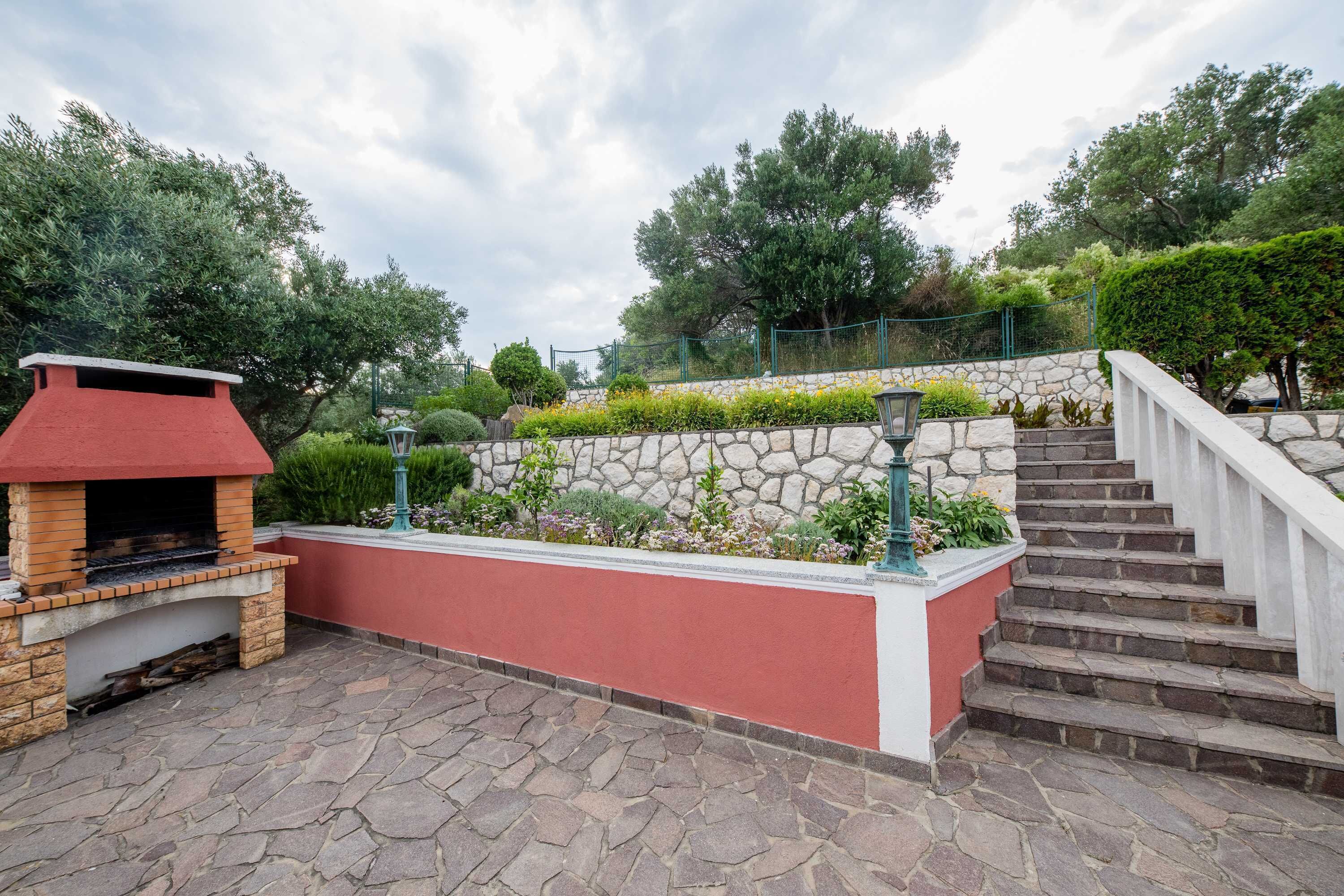 A stone staircase leading up to a red wall with a brick barbecue grill and a stone wall with plants.