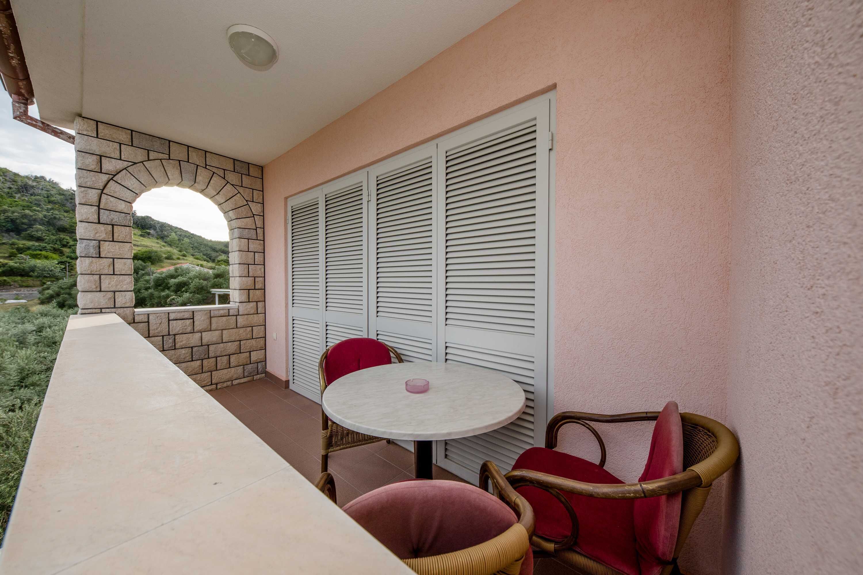 A balcony with a table and chairs, a stone archway, and white shutters.