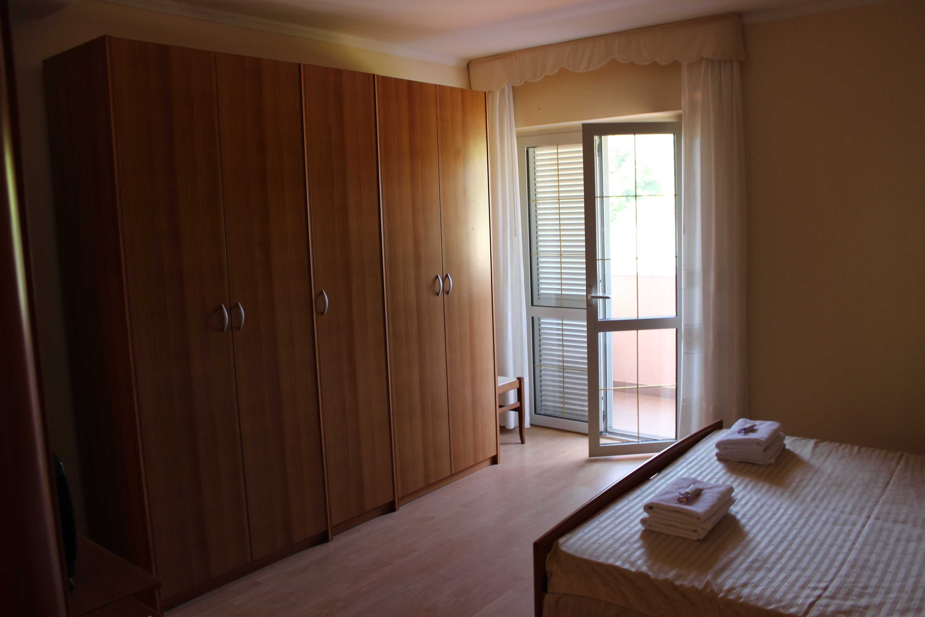 Une chambre à coucher avec un lit, une armoire en bois et une porte-fenêtre coulissante donnant sur un balcon.