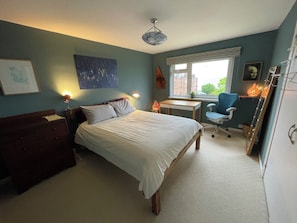 A bedroom with a bed, desk, chair, and a window with a view of buildings.