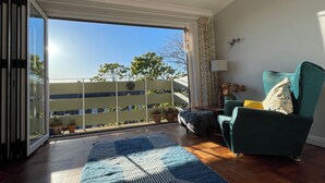 Un soggiorno con una porta scorrevole in vetro che dà su un balcone, una poltrona verde, un tappeto decorato e una lampada.