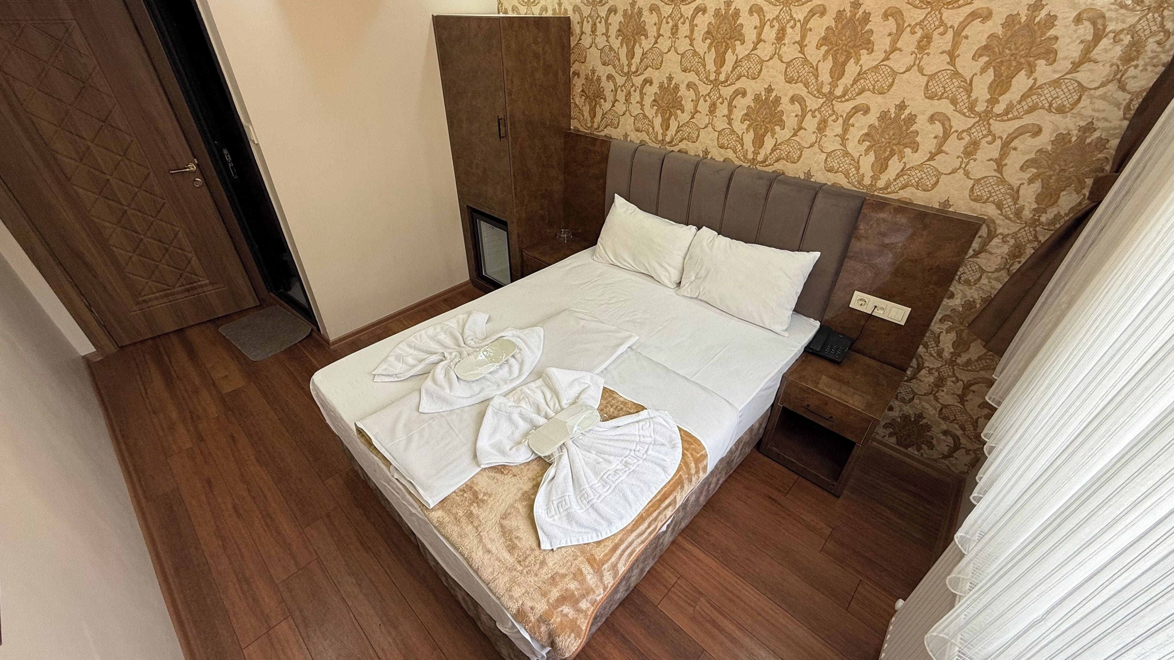 Una habitación de hotel con una cama, un armario, una mesita de noche con teléfono y una pared con diseño.