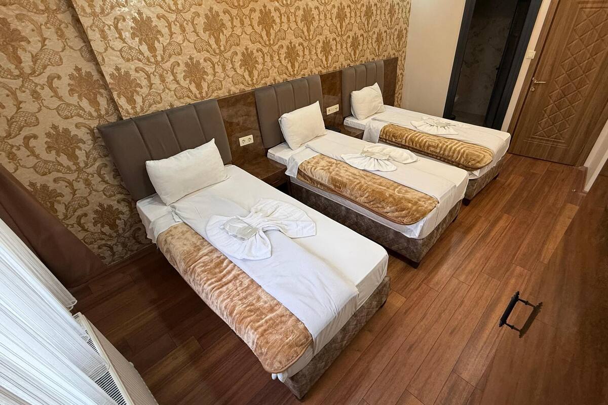 A hotel room with three beds, a patterned wallpaper, and a wooden floor.
