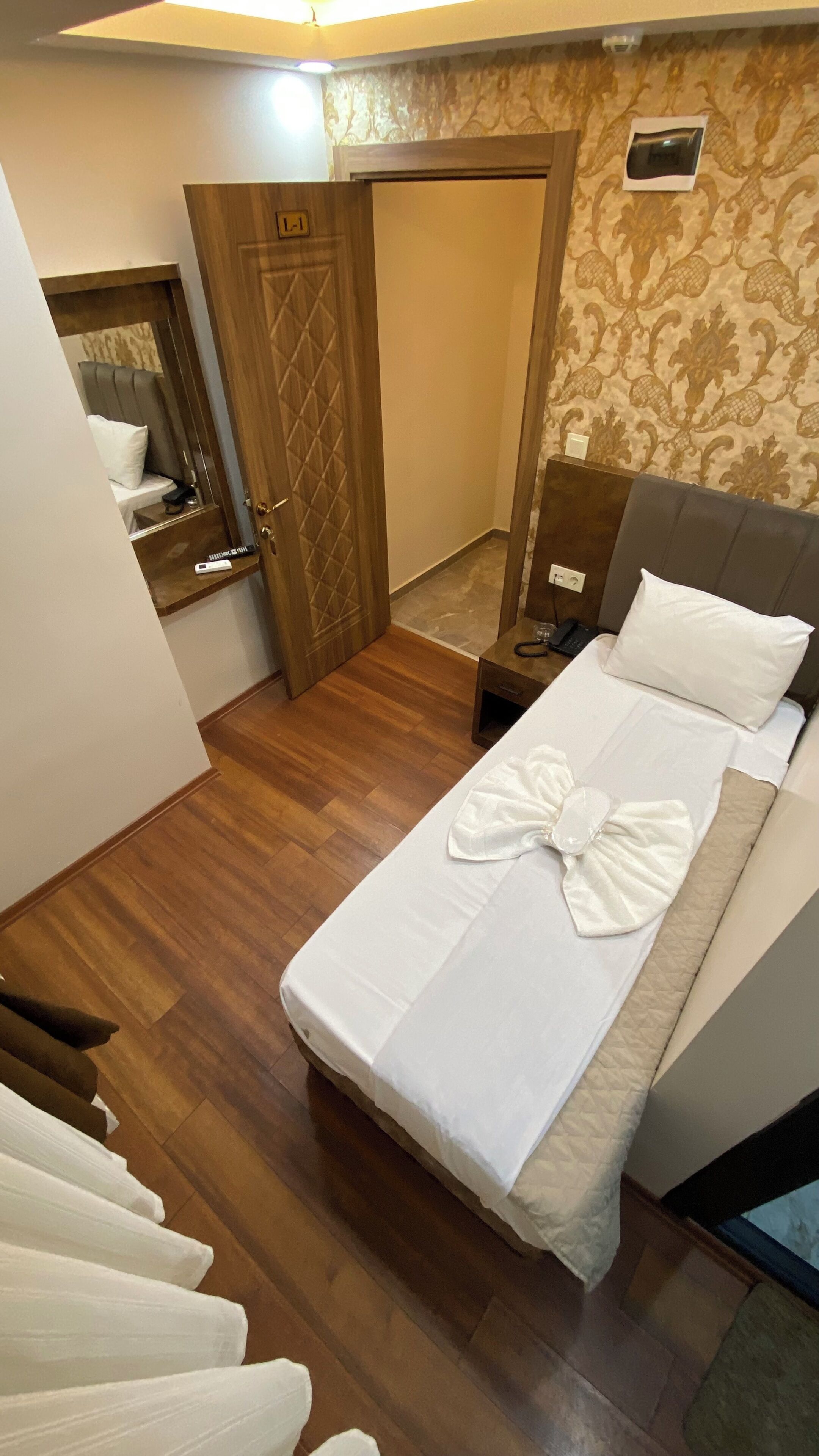 Ein Hotelzimmer mit Bett, Nachttisch, Spiegel, Tür und einer Wand mit Muster.